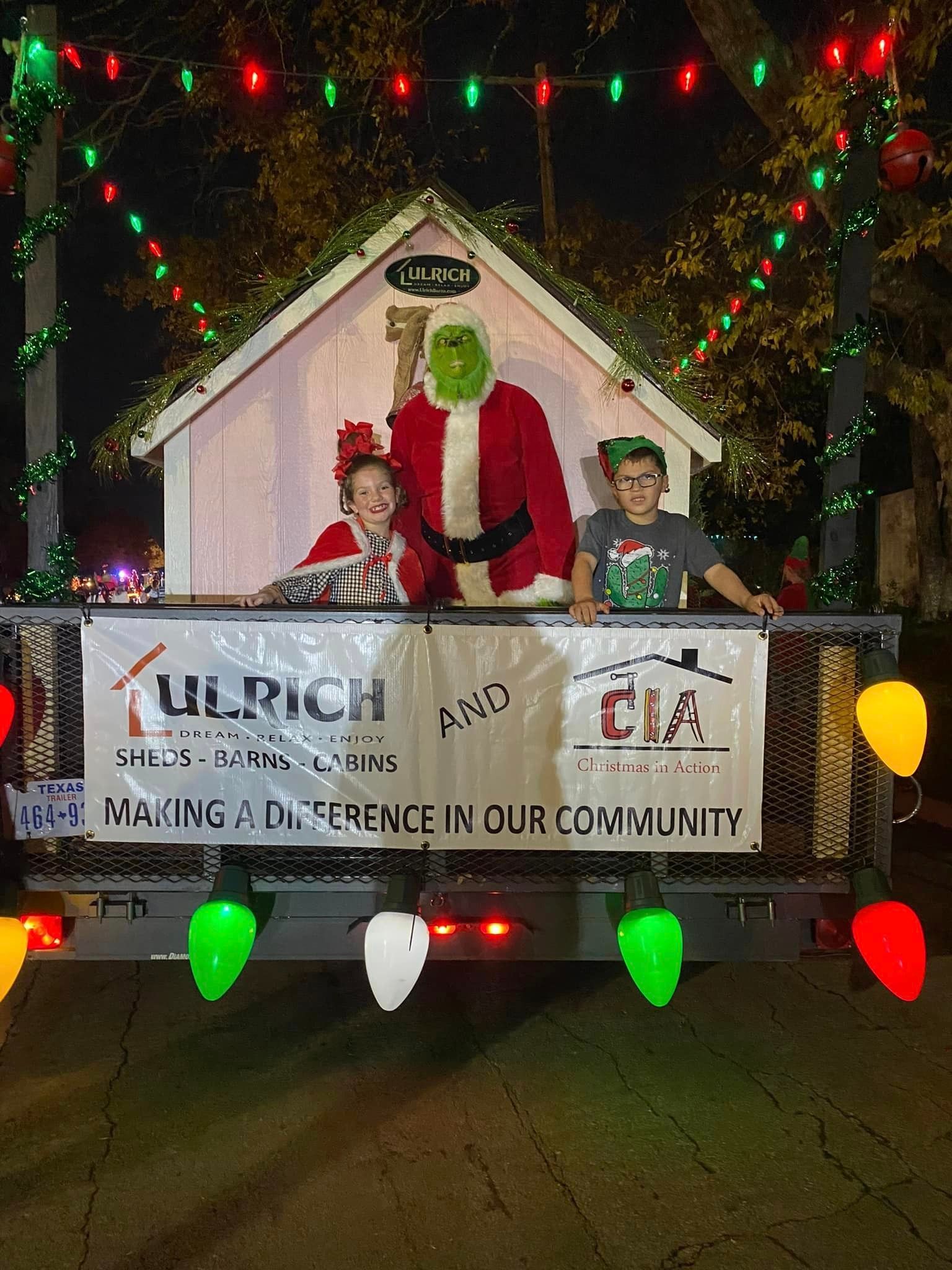 Santa and an elf on a decorated holiday float with colorful lights and sponsor banners