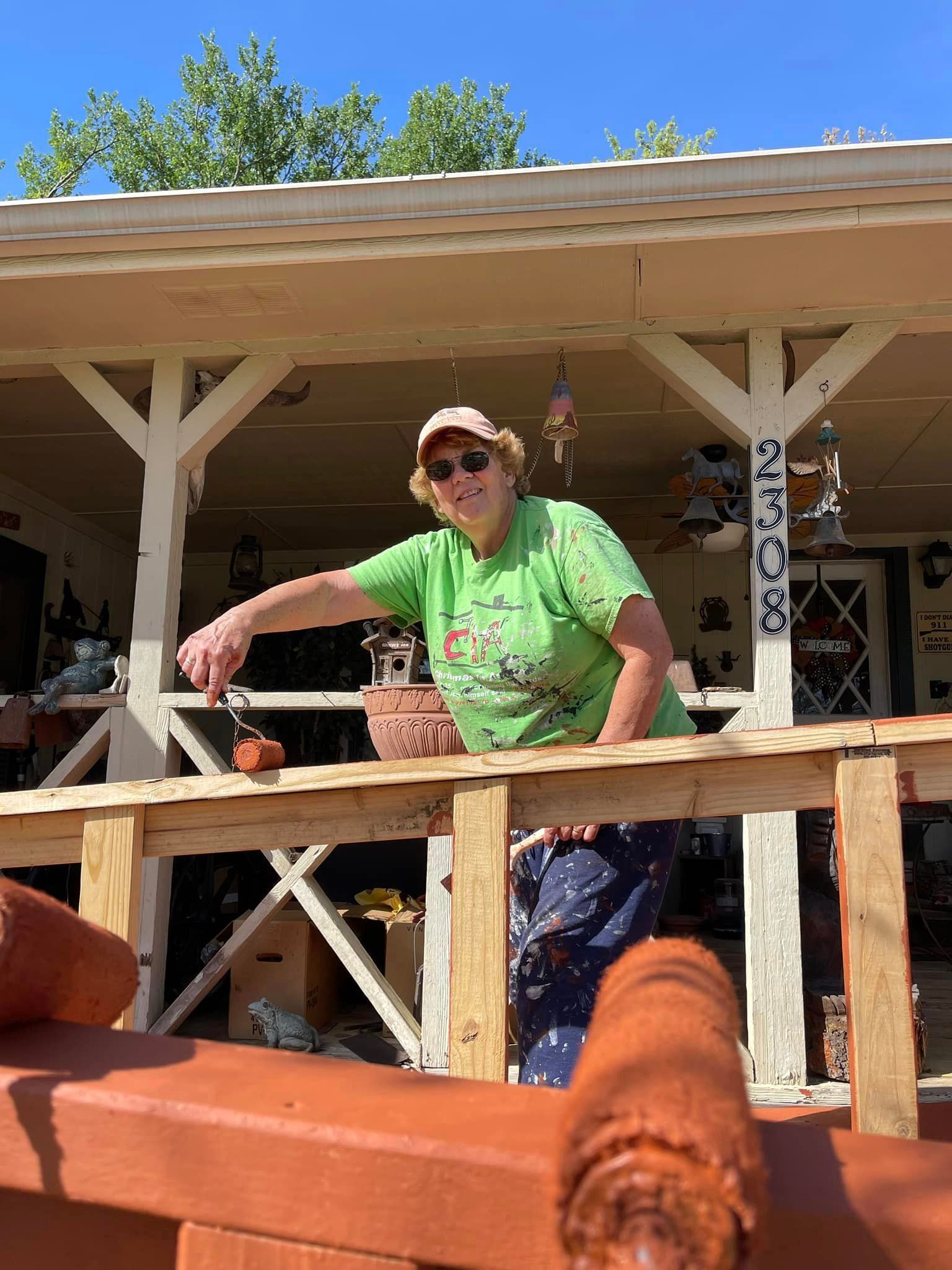 Person in green shirt leaning on a wooden porch railing in bright sunlight