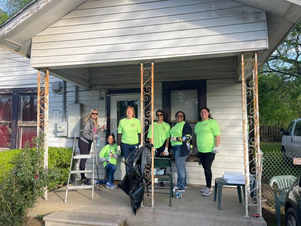 Group in neon green shirts posing on a front porch under renovation, with ladder and tools visible