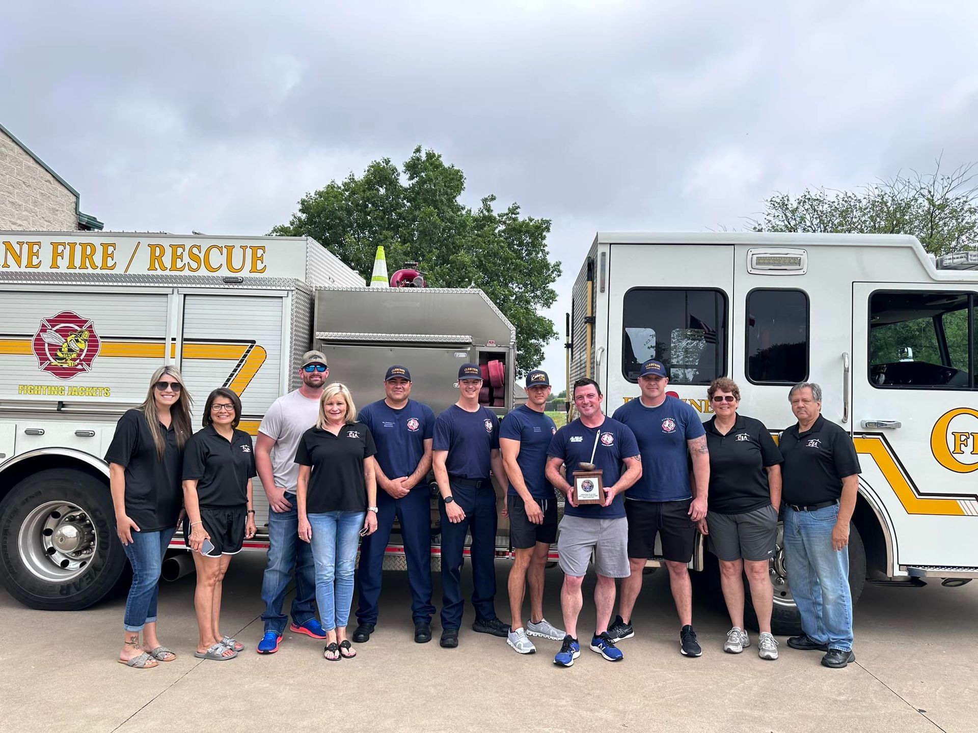 Fire rescue crew posing in front of two fire trucks, standing together outdoors.