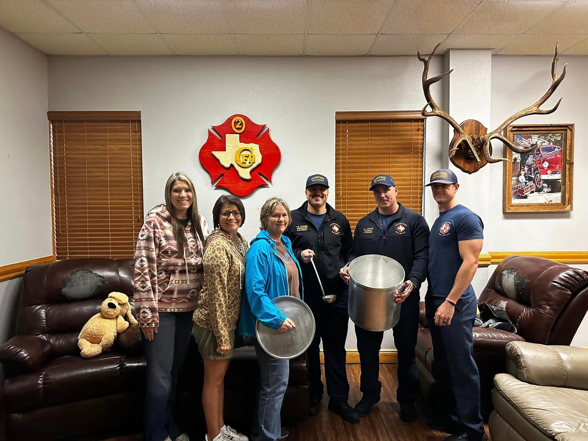Five people holding metal bowls in a lodge-like room with leather couches and mounted antlers.