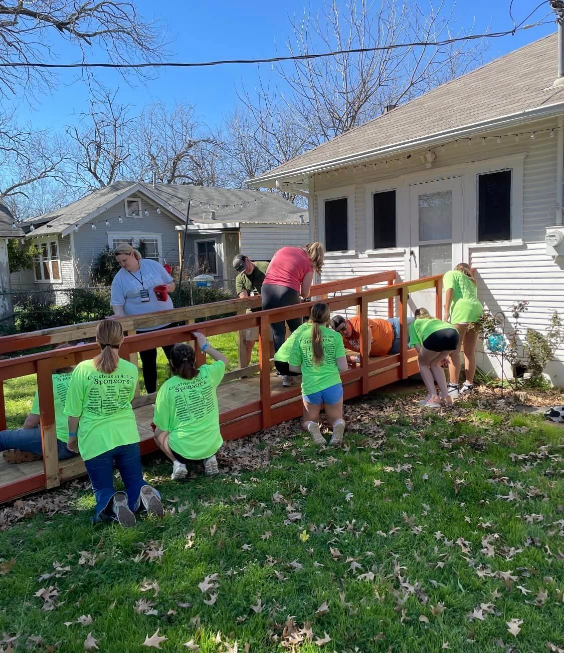 Volunteers building a wooden ramp beside a house on a sunny day