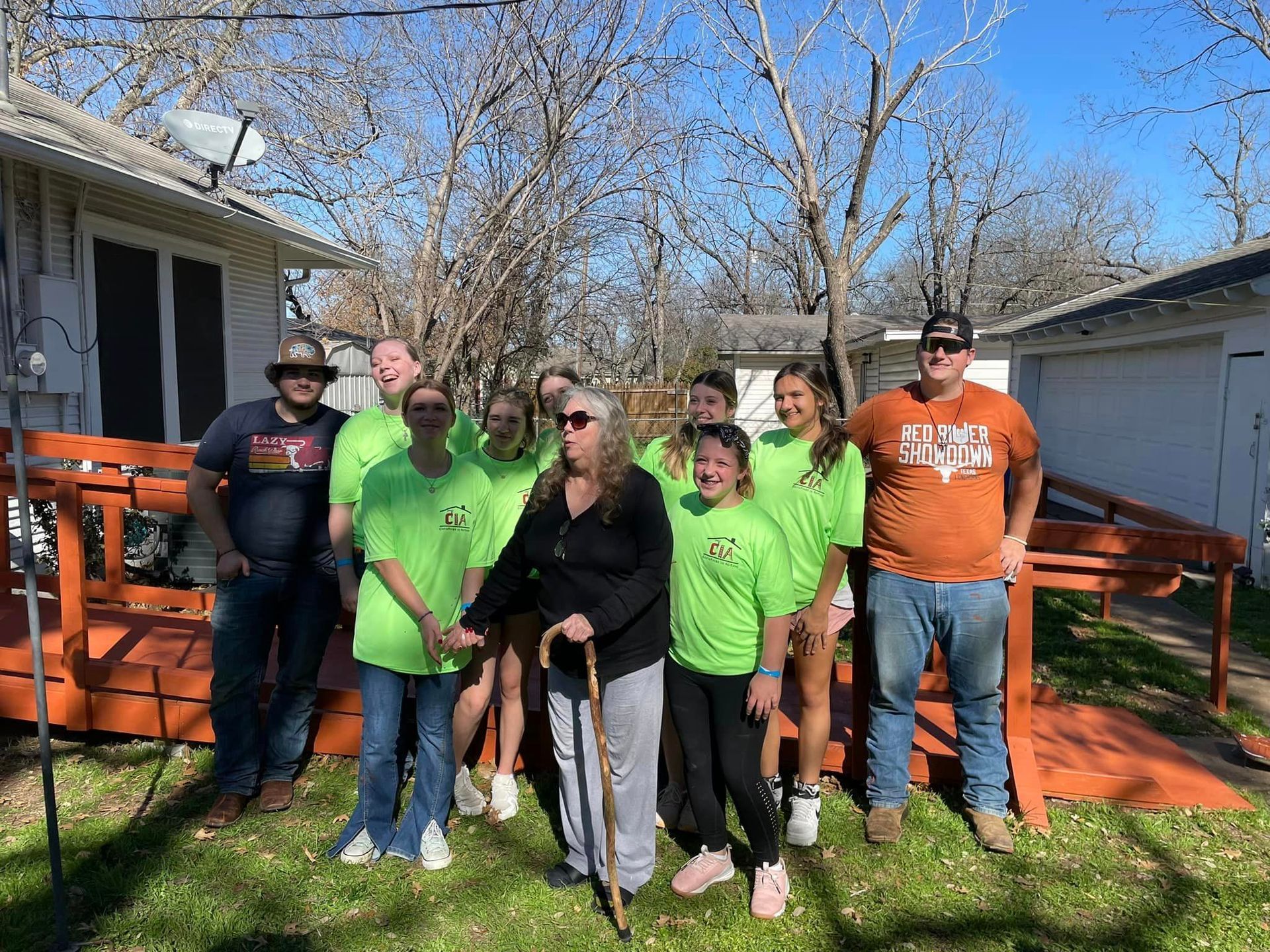 Group posing outdoors by a house and orange ramp, with two bright green shirts and a black dog in front