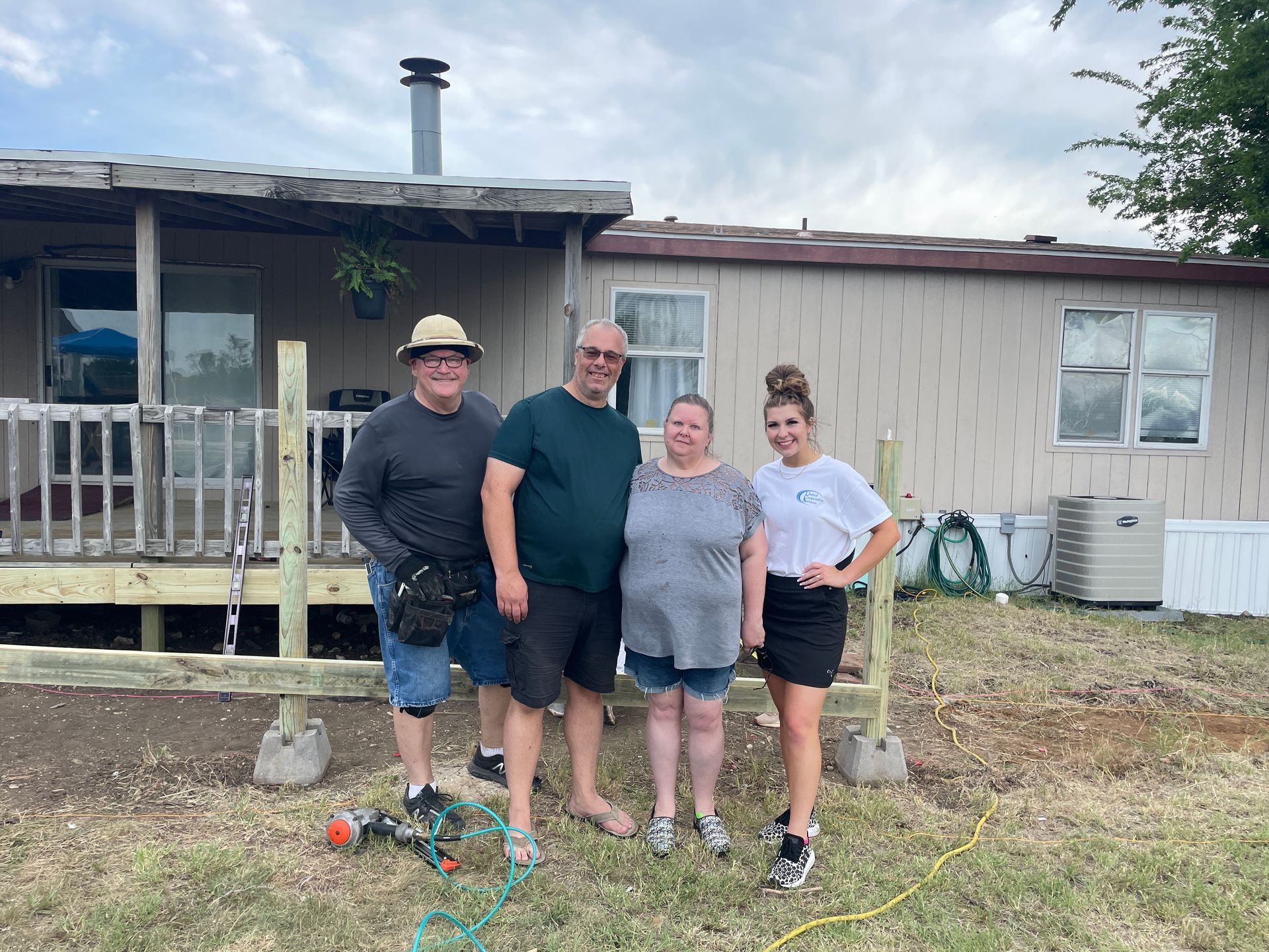 Four people standing together in front of a house, smiling at the camera.