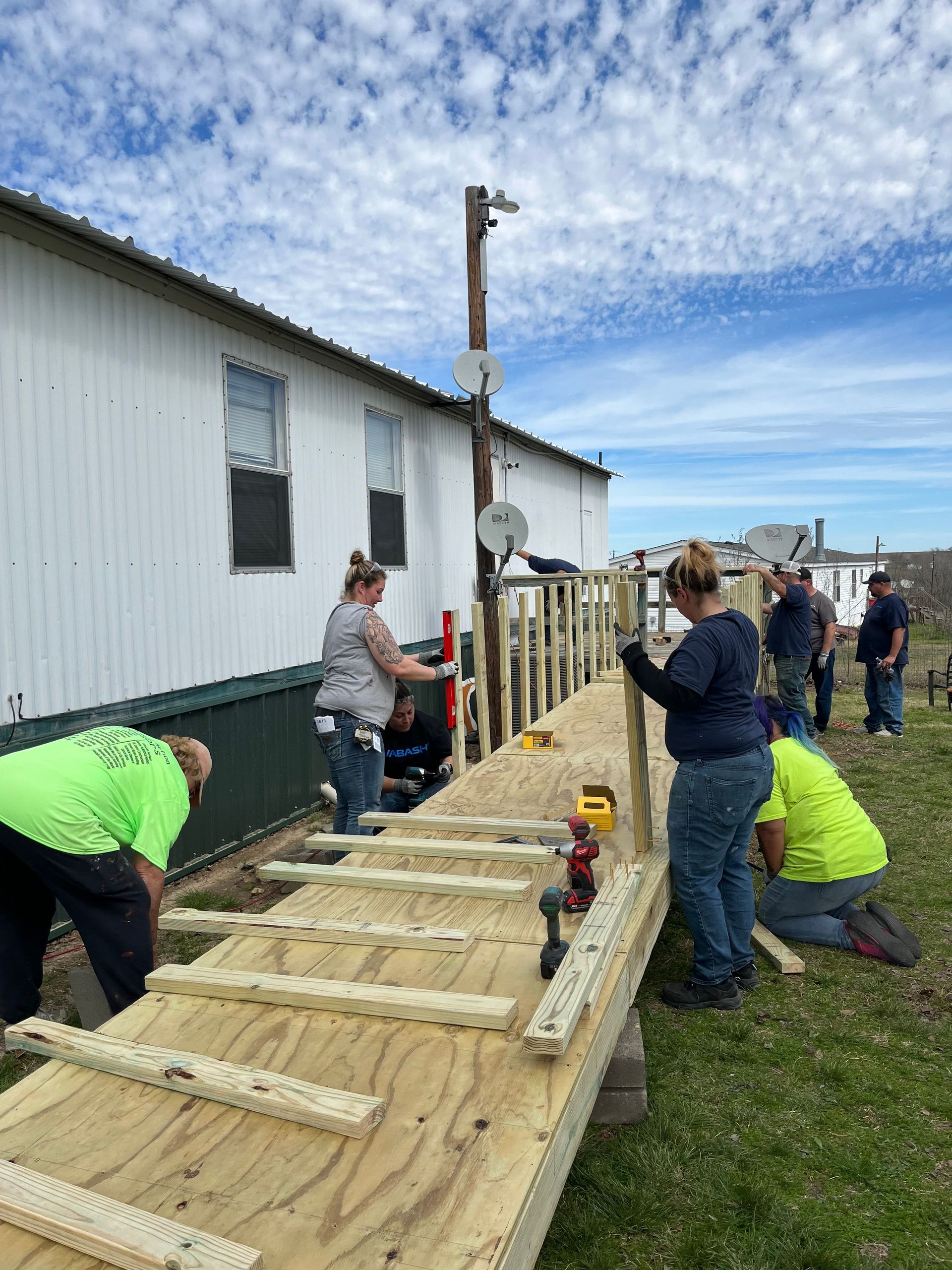 People assembling a wooden ramp beside a white building under a cloudy sky.