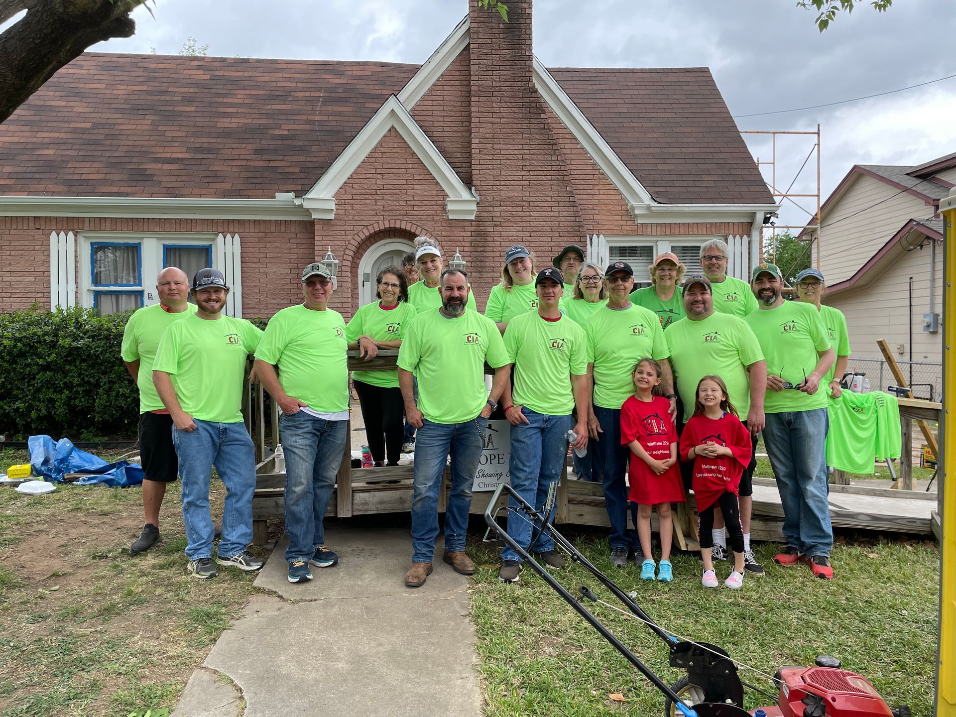 Group in bright green shirts posing outside a brick house, with children in red shirts at the front.