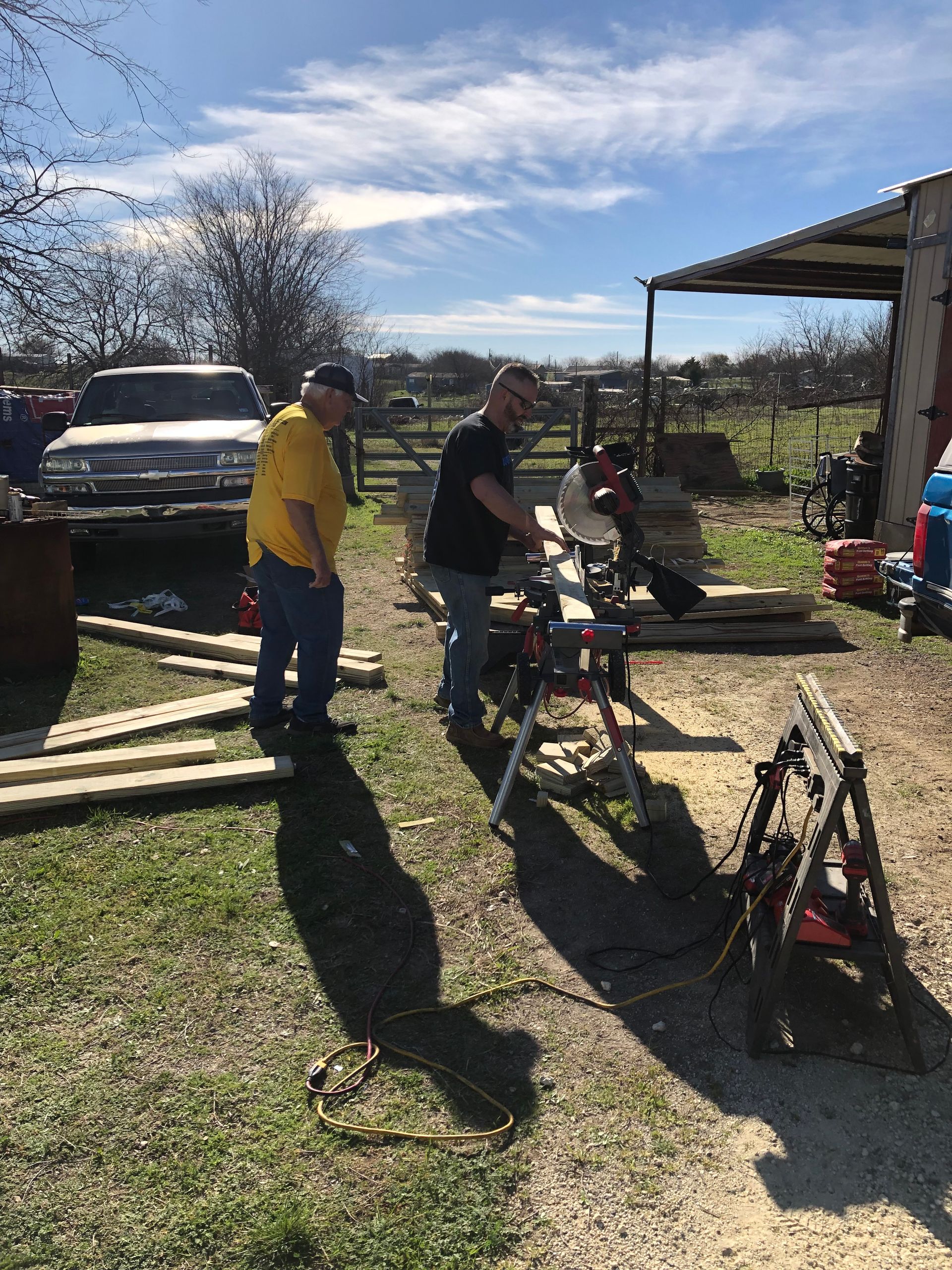 Two people by bicycles in a sunny yard near a parked truck and a covered structure
