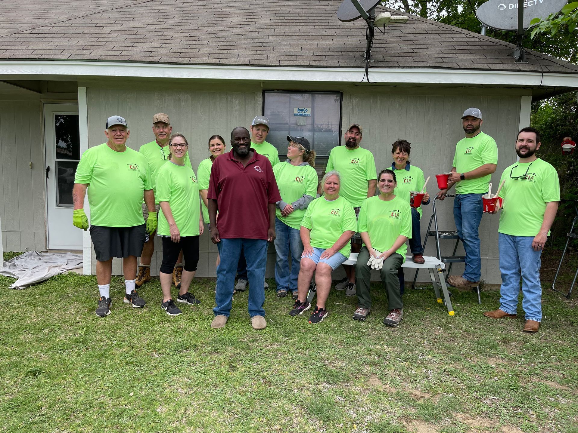 Group of people in neon green shirts posing outside a house, holding red cups and a chair
