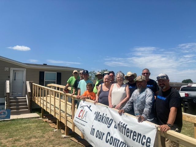 Group of volunteers posing by a ramp with a “Making a difference” banner outside a house
